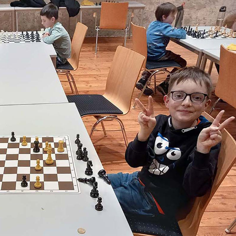 Der Junge gibt beim Schachspielen das Friedenszeichen